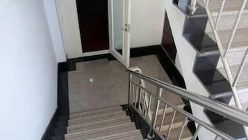 A staircase with a metal handrail and carpeted steps leading to a room with a door.