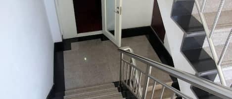 A staircase with a metal handrail and carpeted steps leading to a room with a door.