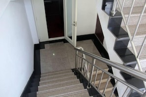 Un escalier avec une rampe métallique et des marches recouvertes de moquette, menant à une pièce dotée d’une porte.