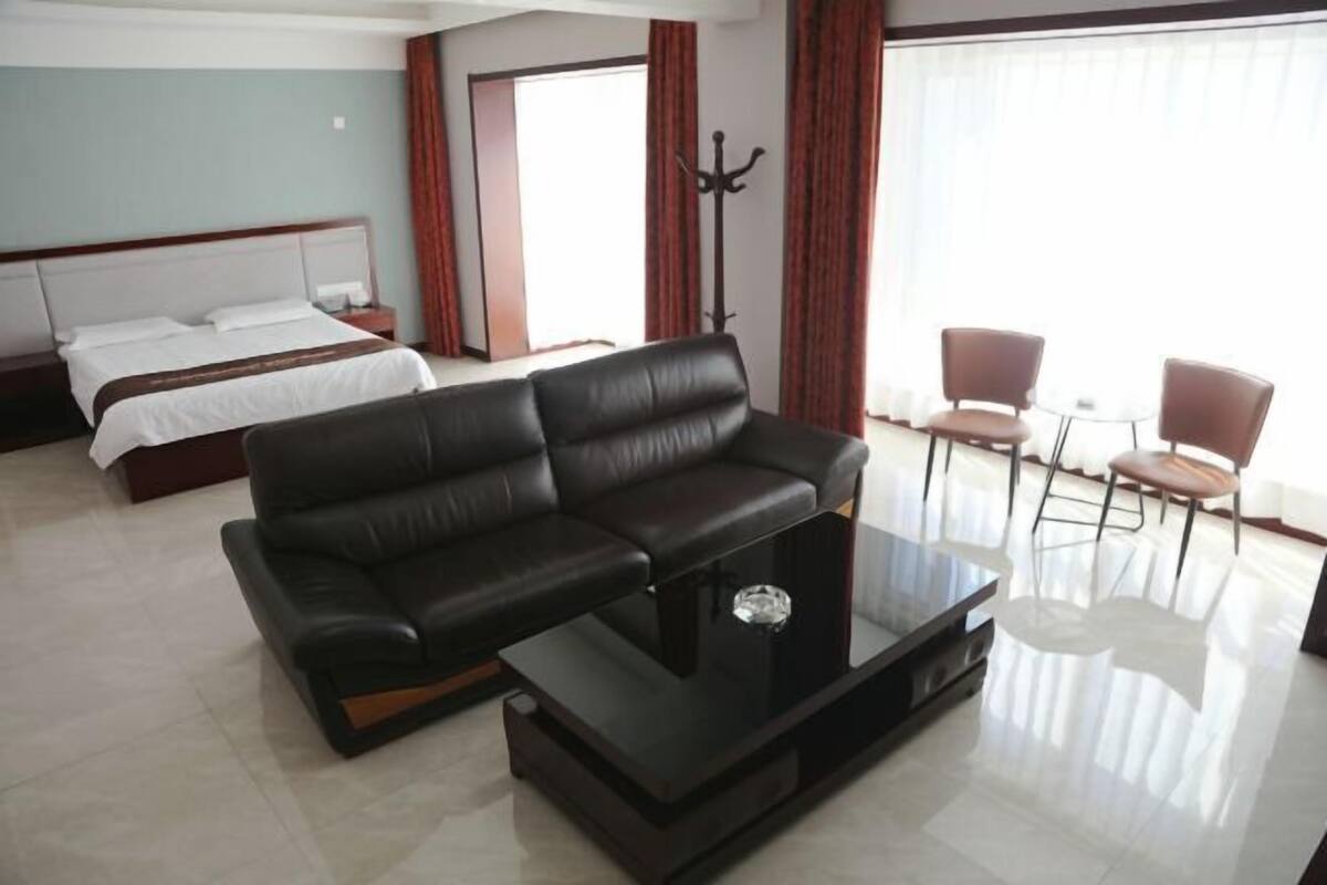 Quarto de hotel com uma cama, um sofá de couro preto, uma mesa de centro de vidro e duas cadeiras.