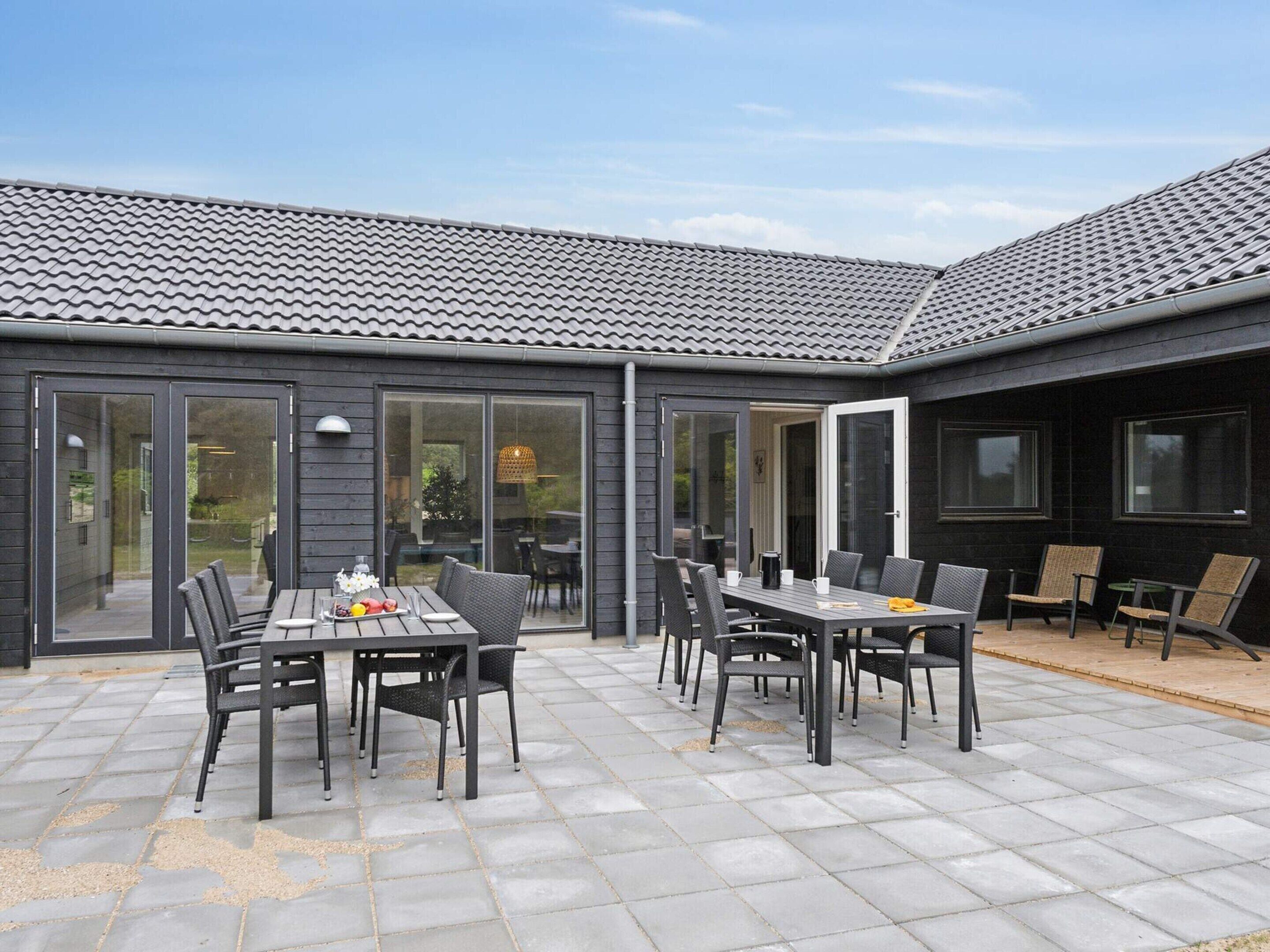 Eine moderne Terrasse mit Ziegeldach, einem Esstisch mit Stühlen und einer Sitzecke mit Tisch und Sesseln.