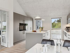 A modern kitchen with built-in appliances, a dining area with a table and chairs, and a view of the outdoors. - 5 Star Holiday Home in Lokken (Lokken)