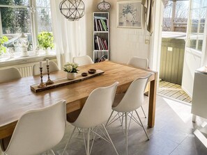 Un coin repas avec une table en bois, des chaises blanches, une bibliothèque et une fenêtre avec des rideaux.