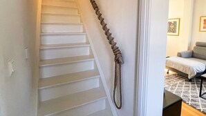 A staircase with a rope handrail, leading to a room with a bed and a patterned rug. - 4 Star Holiday Home in Ronneby (Ronneby)