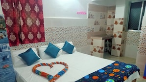 Un dormitorio con una cama, almohadas, una manta colorida, una cortina y una pequeña zona de escritorio.