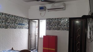 Una habitación con una cama, un armario rojo, una ventana con reja metálica y un equipo de aire acondicionado.