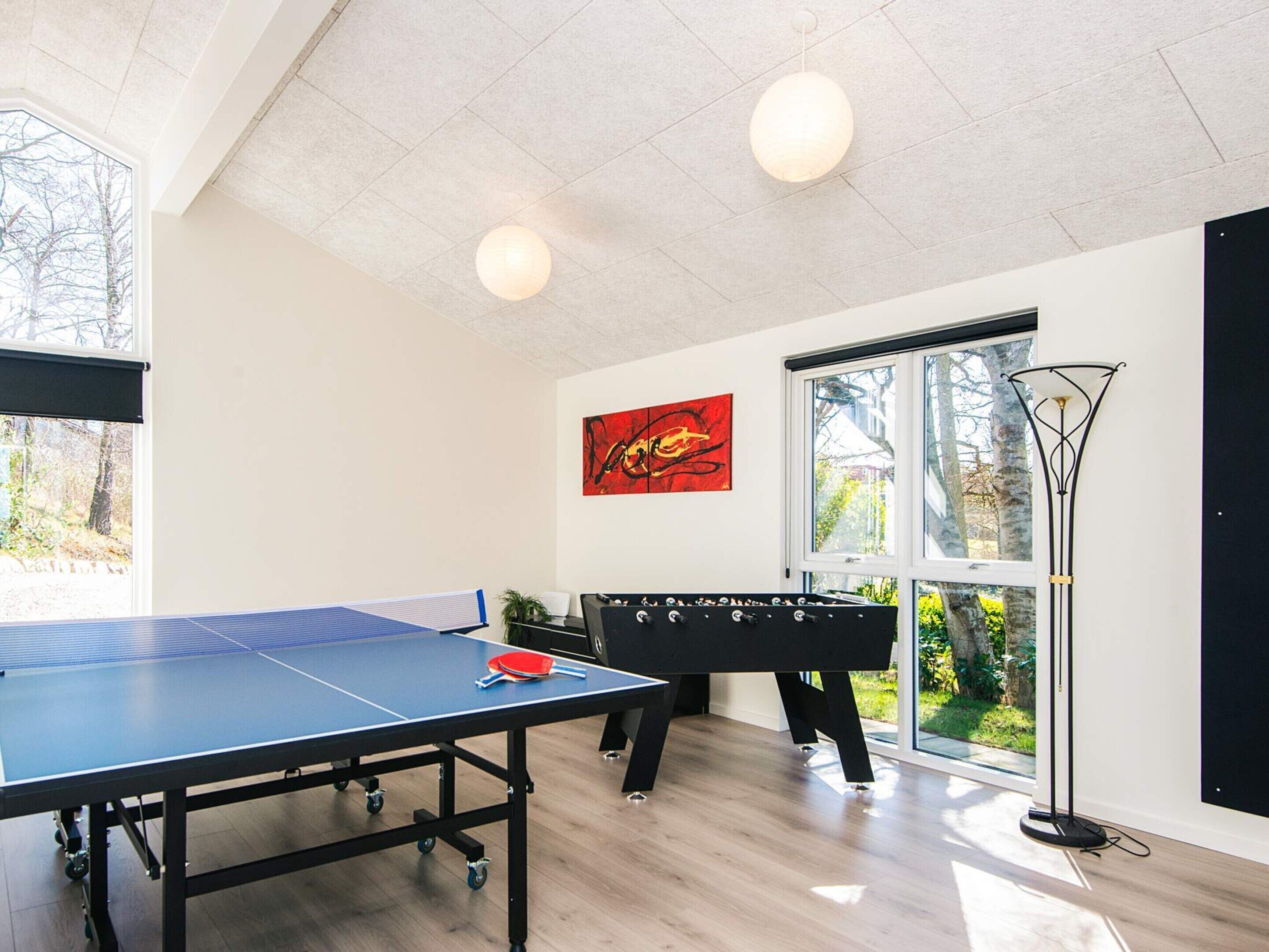Ein Tischtennis-Tisch in einem Raum mit einem großen Fenster, einem schwarzen Sofa und einem roten, abstrakten Gemälde.
