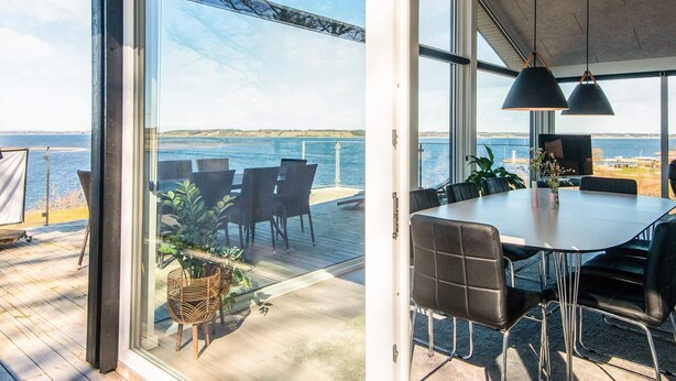 A modern dining area with a large table and chairs, overlooking a body of water. - 5 Star Holiday Home in Logstrup (Logstrup)
