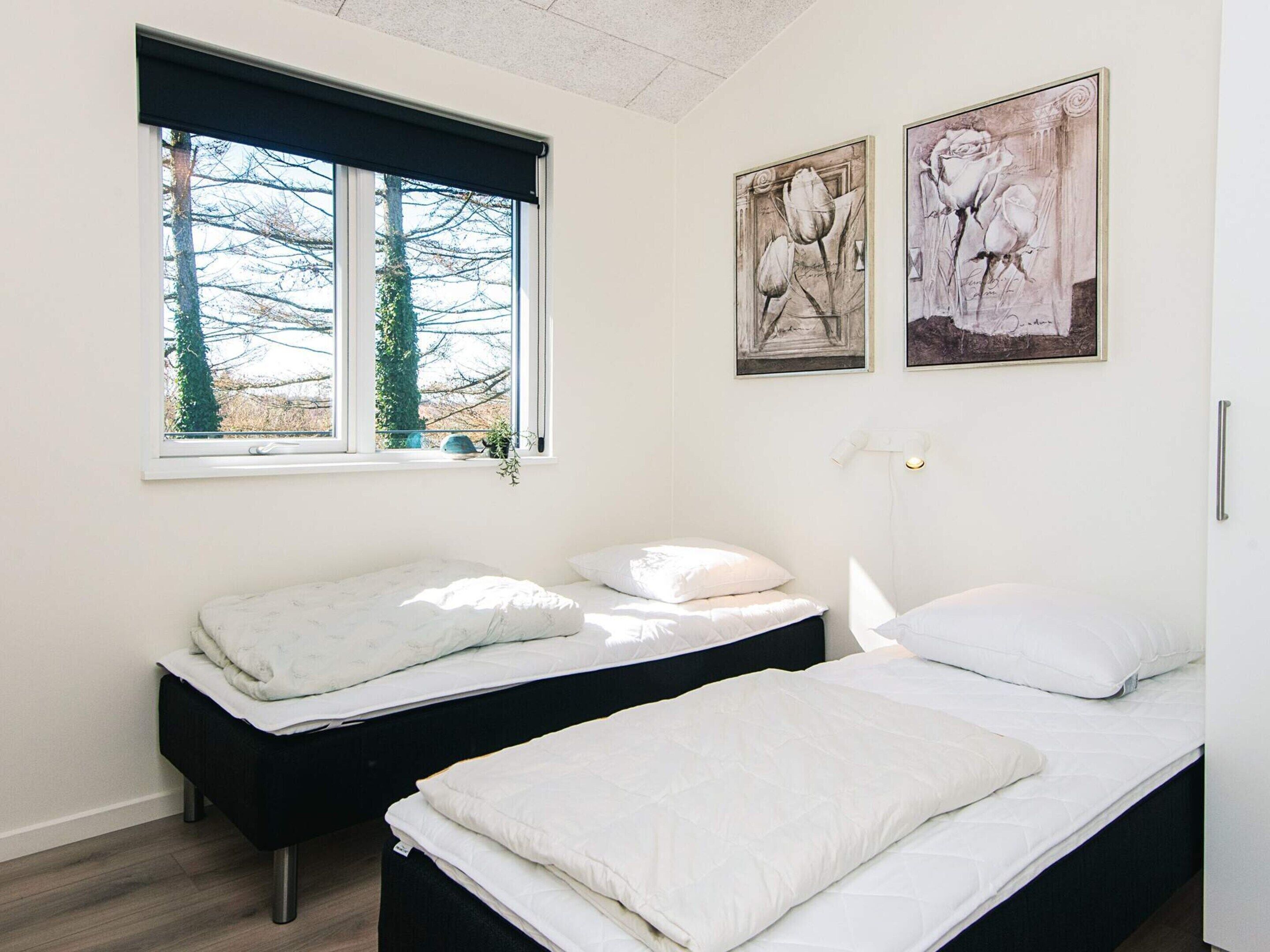 A bedroom with two single beds, a window with a view of trees, and two framed artworks on the wall.