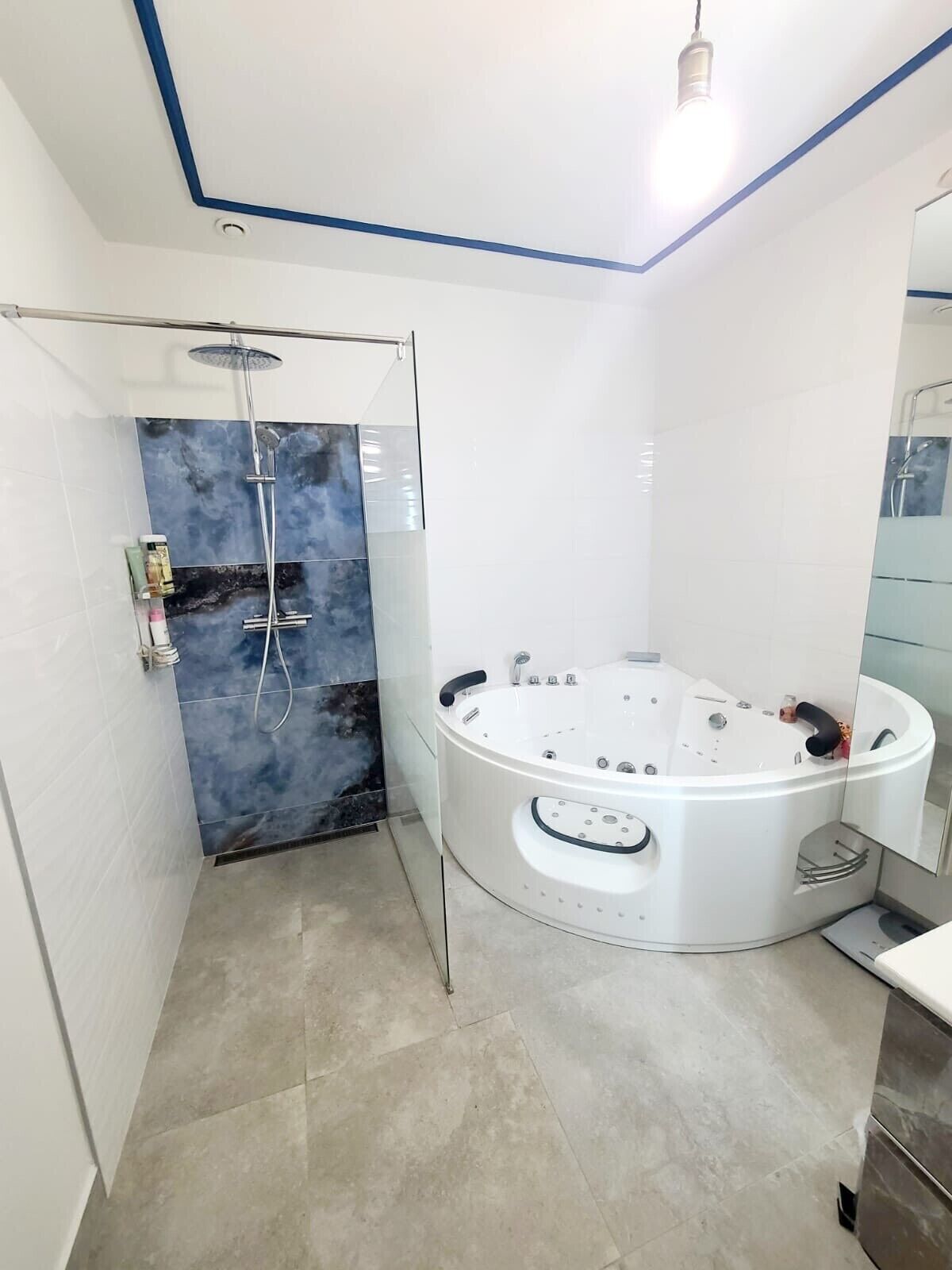 Een moderne badkamer met een glazen douchecabine, een witte badkuip en een grote spiegel.