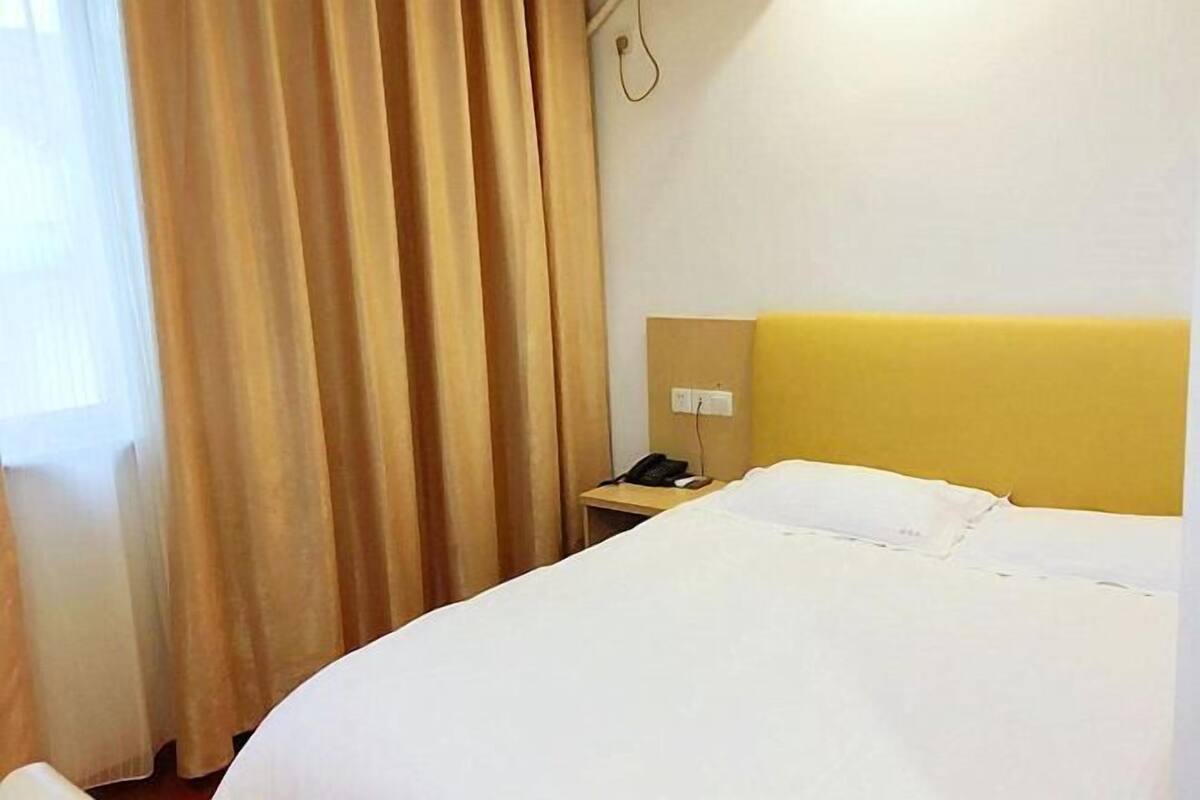 A hotel room with a bed, a nightstand with a phone, and a wall-mounted light fixture.