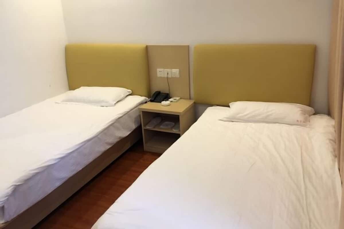 A hotel room with two single beds, a bedside table with a phone and a lamp, and a wall socket.