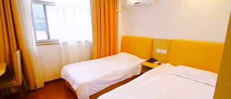 Habitación de hotel con dos camas individuales, un escritorio, una silla, un ventanal con cortinas y un equipo de aire acondicionado.