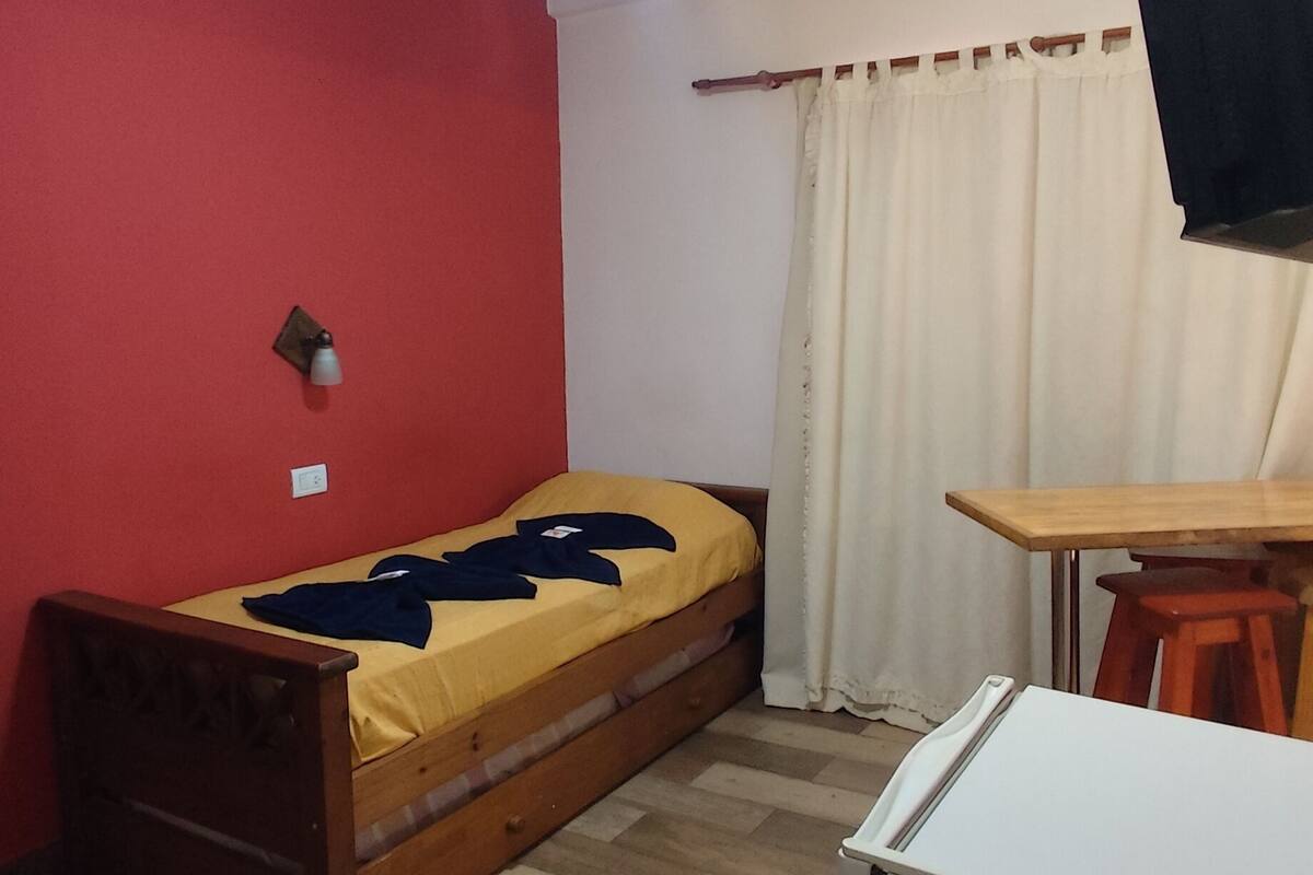 A compact room with a bed, a desk, a ceiling fan, and a television.