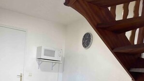 A dining area with a table set for two, a microwave above the table, and a clock on the wall. - Typical little house in the village of Piana (Piana)