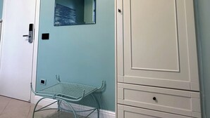 Une pièce avec une porte blanche, un banc en métal, une armoire blanche avec des tiroirs et un miroir fixé au mur.