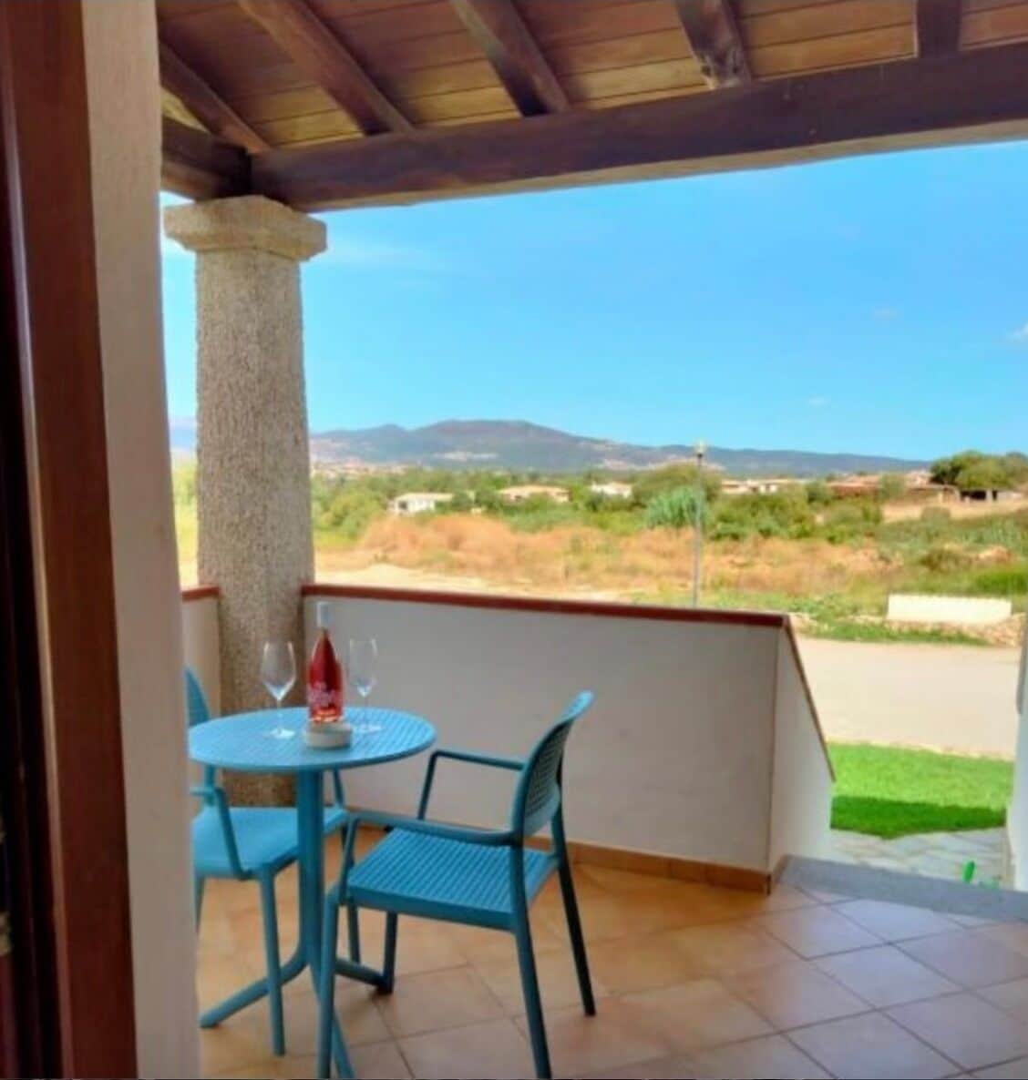 Een overdekt terras met een tafel en stoelen, een uitzicht op het landschap en een heldere lucht.