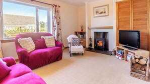 A living room with a sofa, a fireplace, a television, and a window with curtains. - The perfect location to explore the Highlands. (Nairn)