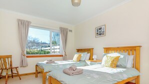 A bedroom with two wooden beds, a window with curtains, a wooden chair, and a small picture on the wall. - The perfect location to explore the Highlands. (Nairn)