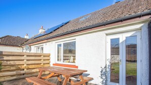 A house with a patio, a wooden table, and a door with glass panels. - The perfect location to explore the Highlands. (Nairn)