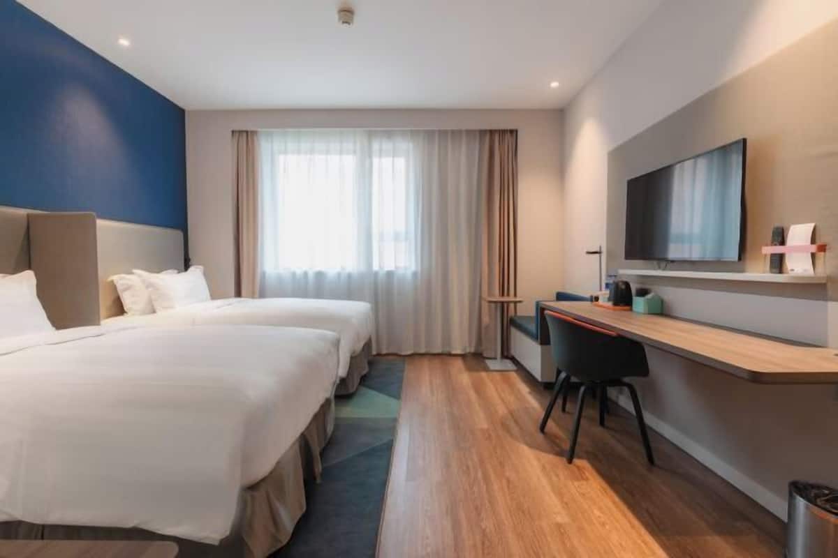 Habitación de hotel con dos camas, un escritorio, un televisor y una ventana con cortinas.