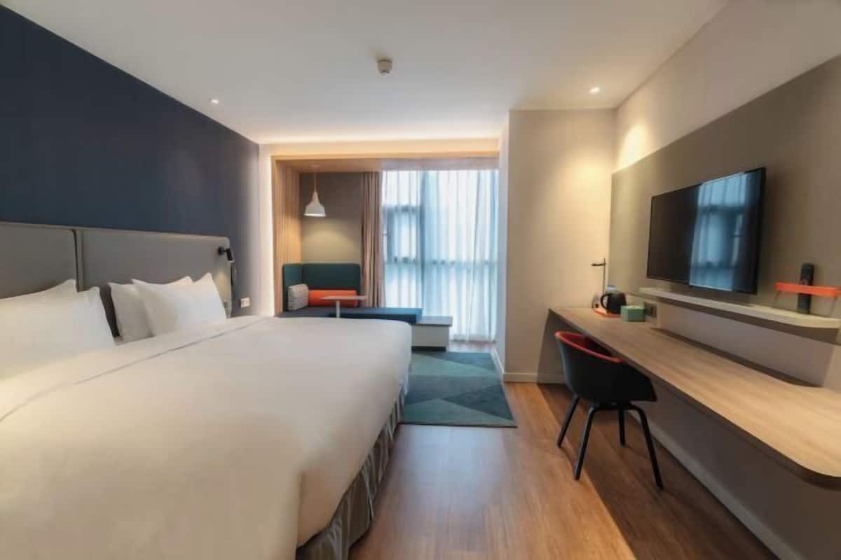 Habitación de hotel con cama, escritorio, televisor y ventana con cortinas.