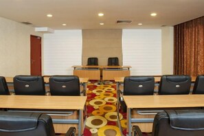 Une salle de conférence avec une longue table, de nombreuses chaises et un tapis orné d’un motif circulaire.