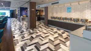 Un hall d’hôtel moderne avec un sol à motifs en chevrons, un comptoir d’accueil et un espace détente avec des fauteuils.