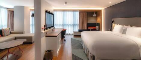 A modern hotel room with a large bed, a desk, a sofa, and a TV.