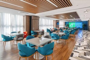 Eine Hotelhalle mit mehreren Sitzbereichen, einem großen Bildschirm mit dem Hotelnamen und einem gemusterten Boden.