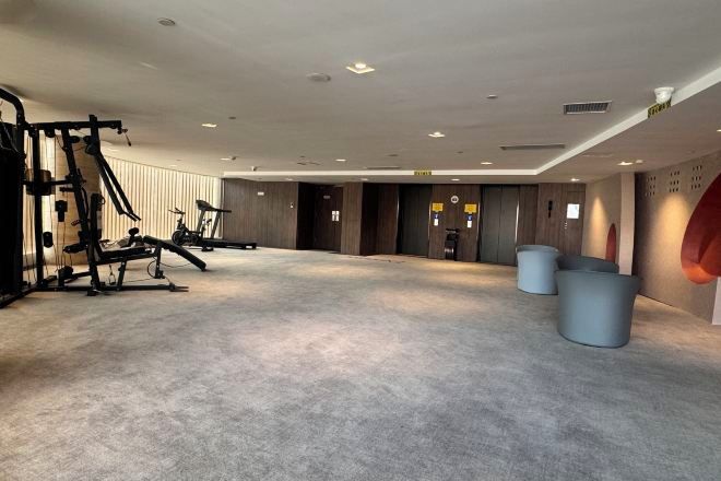 A spacious gym with exercise equipment, a large mirror, and a carpeted floor.
