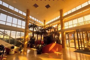 Eine geräumige Lobby mit hohen Decken, großen Fenstern und mehreren Palmen.