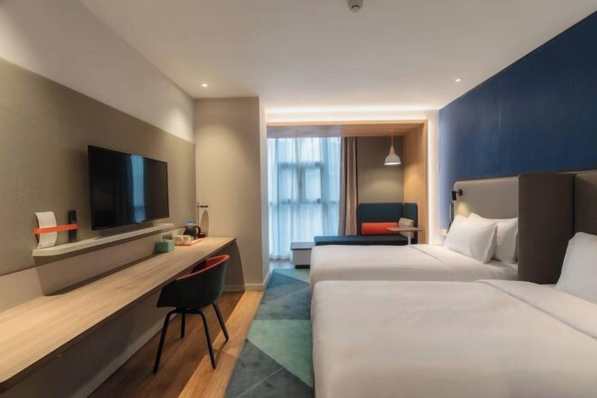 Habitación de hotel con televisión, escritorio, dos camas y ventana con cortinas.
