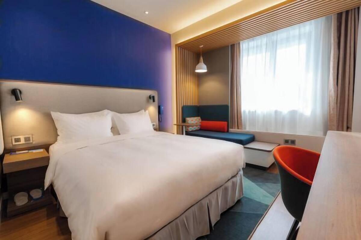 Una habitación de hotel con una cama grande, una mesita de noche, una silla, una pequeña mesa y una ventana con cortinas.