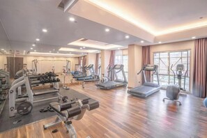 Een ruime fitnessruimte met diverse trainingsapparaten, grote ramen en een houten vloer.