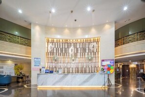 Un espace d’accueil d’hôtel avec un comptoir en marbre, un panneau d’affichage numérique et un mur décoratif.