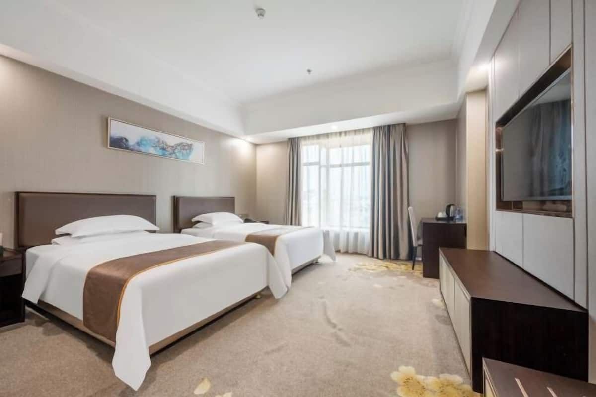 Une chambre d’hôtel avec deux lits, un téléviseur à écran plat, un bureau et une grande fenêtre avec des rideaux.