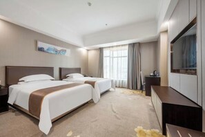 Een hotelkamer met twee bedden, een flatscreen televisie, een bureau en een groot raam met gordijnen.