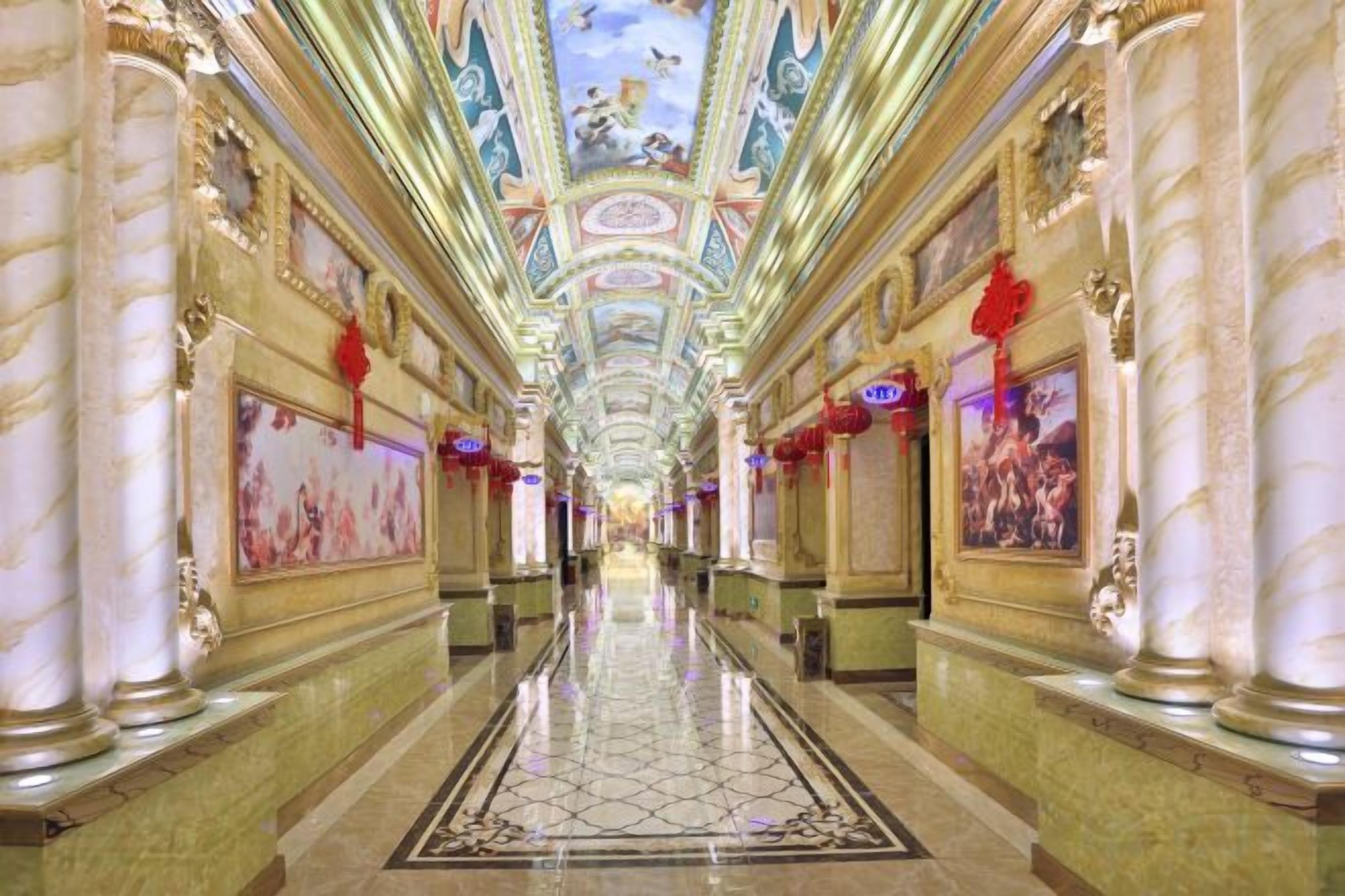A long, ornate hotel corridor with marble columns, a tiled floor, and a ceiling with painted artwork.