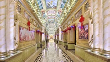 A long, ornate hotel corridor with marble columns, a tiled floor, and a ceiling with painted artwork.