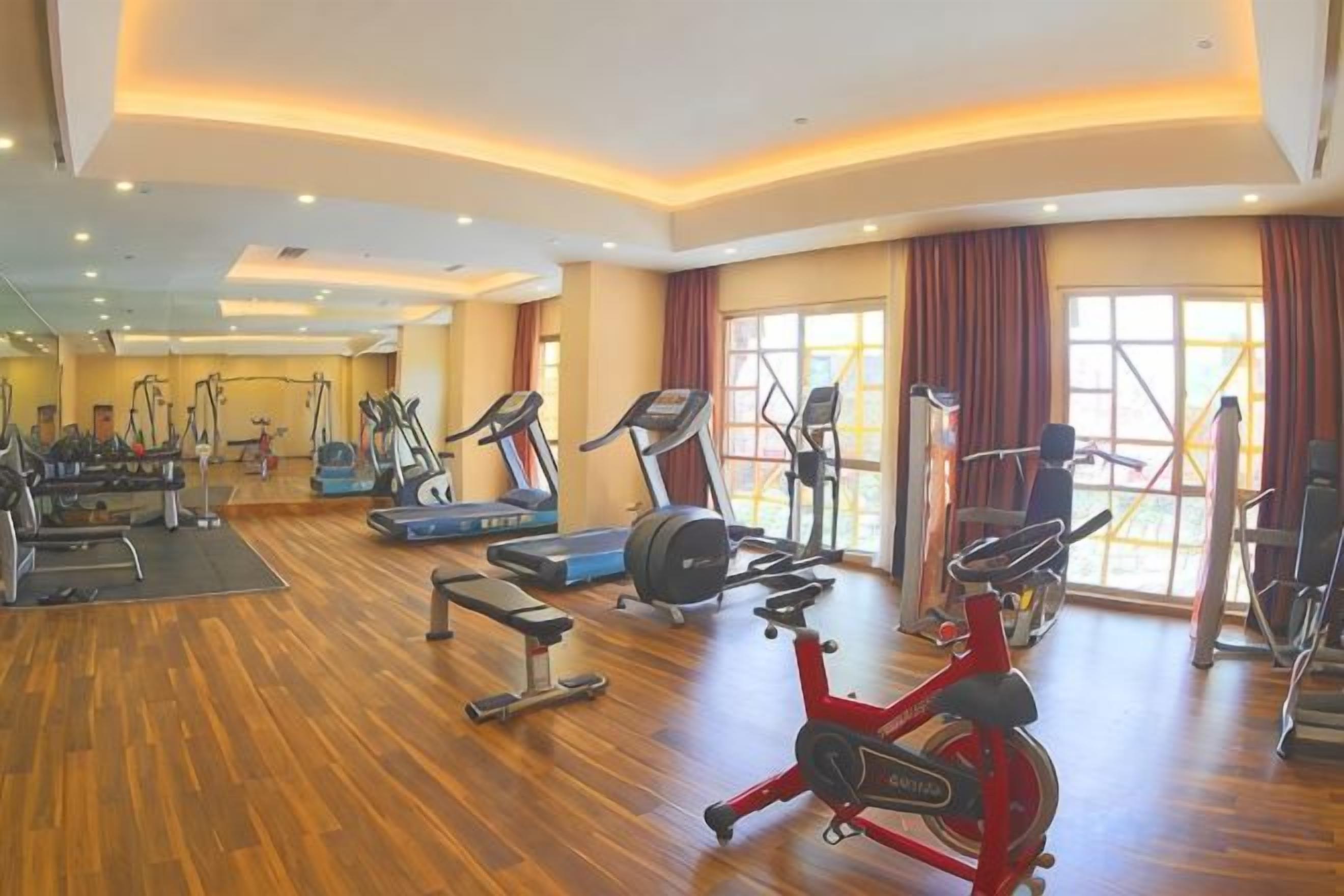 Uma academia ampla com diversas máquinas de cardio, um banco de musculação e um remo.