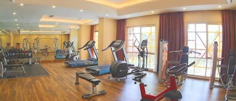 Uma academia ampla com diversas máquinas de cardio, um banco de musculação e um remo.