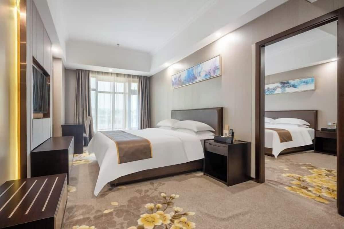 Une chambre d’hôtel avec un grand lit, une table de chevet, une commode, un miroir et une fenêtre avec des rideaux.