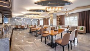 A modern hotel lobby with a central dining area, a reception desk, and a seating area with a sofa and chairs. - Ye Feng Garden Hotel (Dongguan)