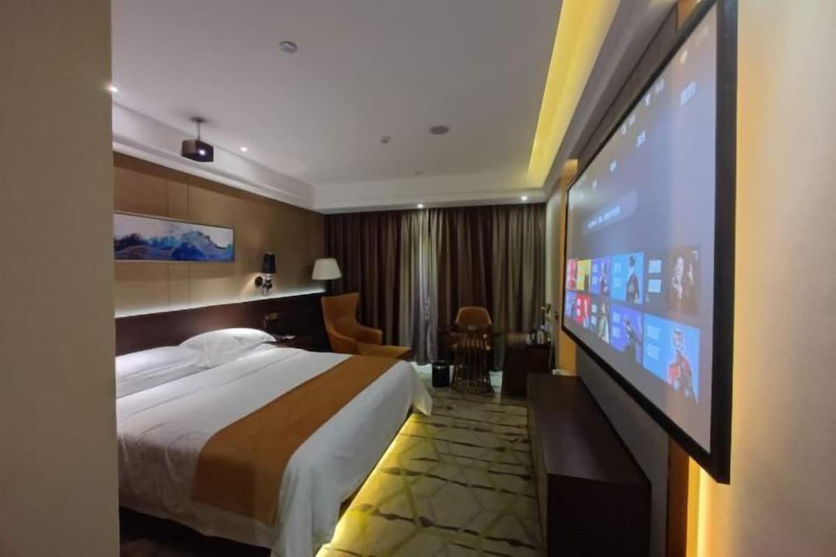 Une chambre d’hôtel avec un lit, un bureau, une chaise, un écran de télévision et un grand tableau accroché au mur.