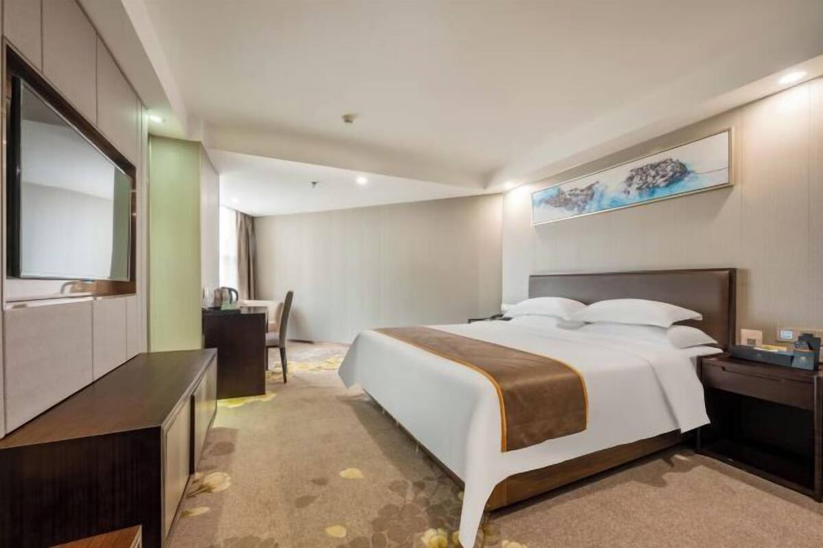 Une chambre d’hôtel avec un grand lit, un bureau, une chaise, une armoire et un tableau au mur.