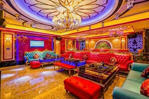 Un hall d’hôtel luxueux, doté de fauteuils confortables, d’un lustre et d’un grand écran.