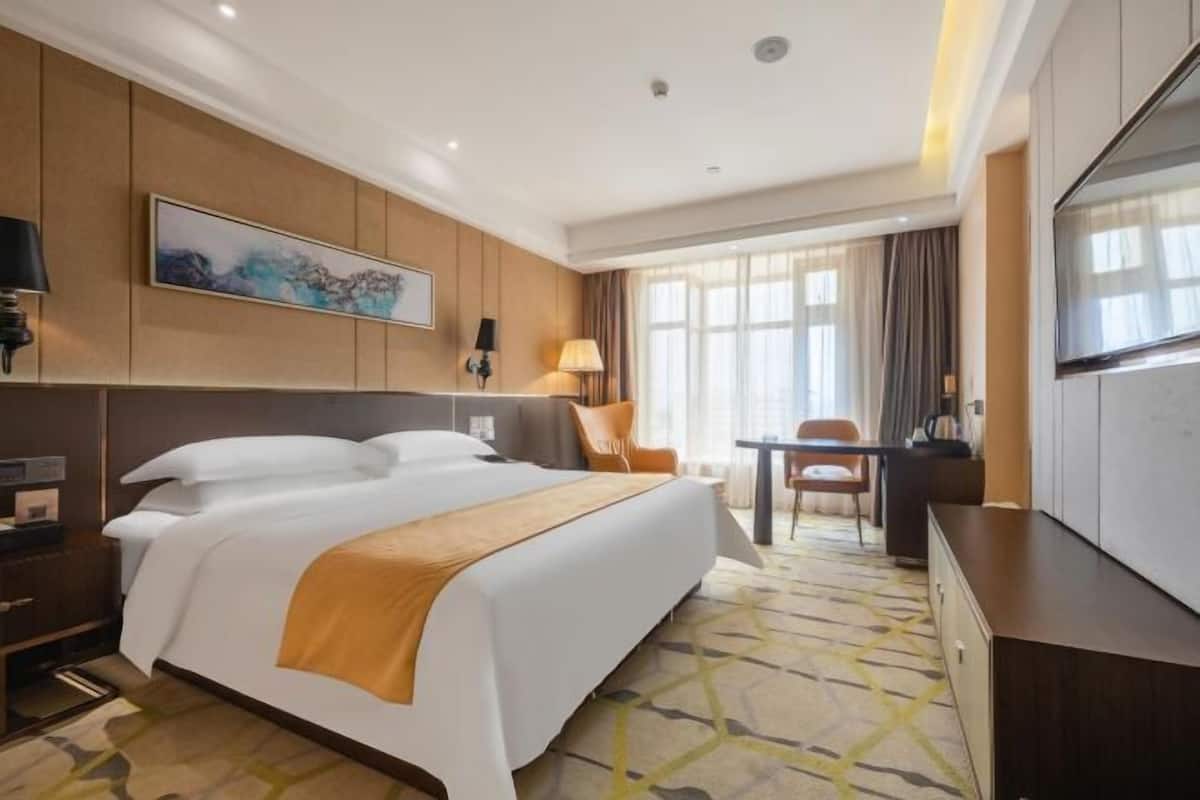 Une chambre d’hôtel avec un grand lit, un bureau, une chaise, une télévision et un tableau au mur.