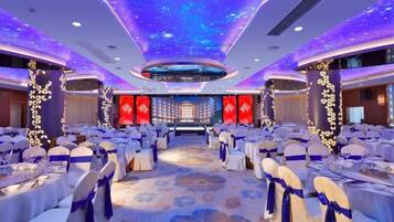 A banquet hall with round tables and chairs, a stage with red curtains, and a ceiling with a starry light display.