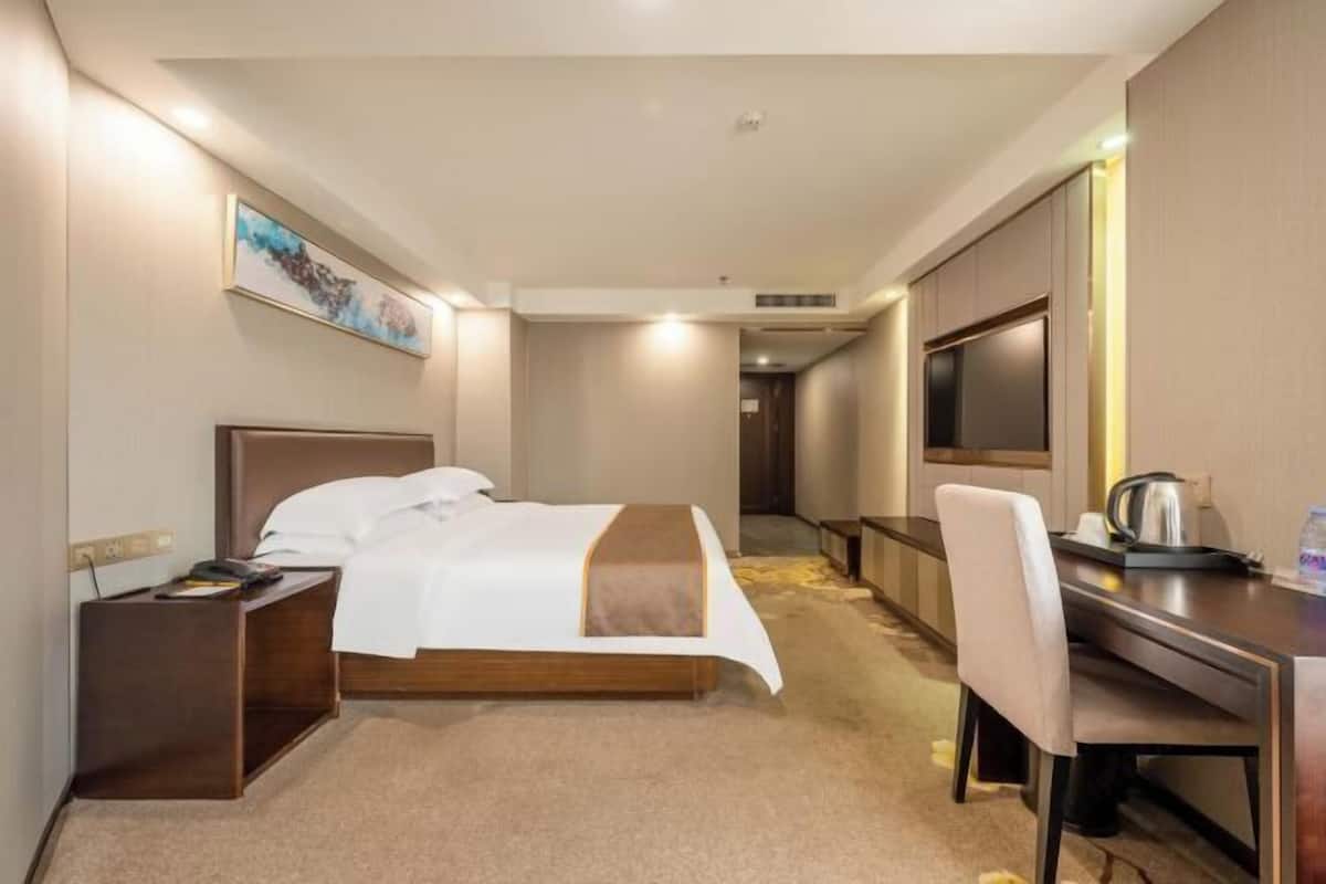 Une chambre d’hôtel avec un lit, un bureau, une chaise, une télévision et un tableau au mur.